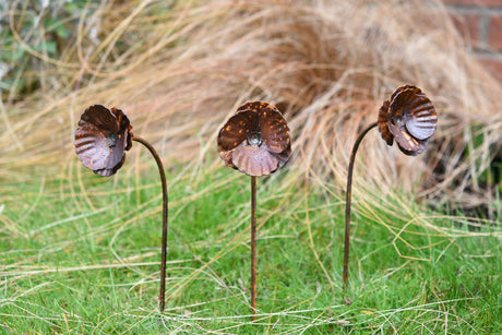 Set of three metal Poppy Flower garden decorations with intricate petal designs on green grass