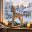 Wooden Rocking Horse Christmas decoration beside candles and greenery on a snow-covered window sill