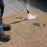Person cleaning a natural jute round rug with a pressure washer for easy maintenance