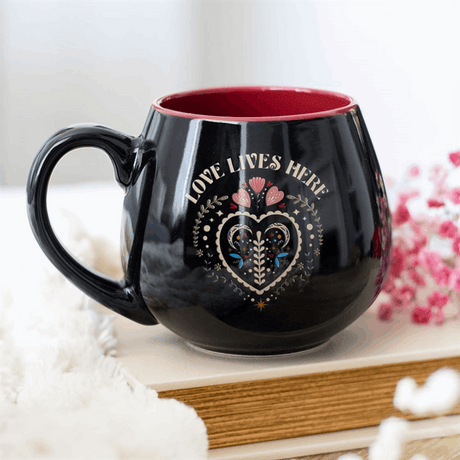 Black Rounded Mug with heart design and the phrase Love Lives Here on a wooden surface