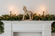 Rustic Rocking Horse decor atop a fireplace mantel adorned with greenery and candles for Christmas room decorations