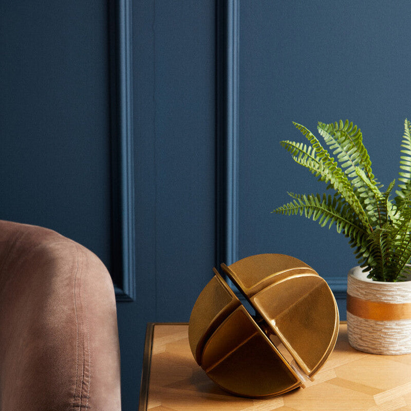 Orsina abstract gold sculpture on a wooden table with a decorative plant in the background