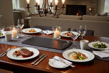 Elegant slate serving tray on a dining table, surrounded by plates of gourmet food