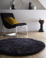 Round Shaggy Rug in dark colour, placed under a chair in a stylish living room setting