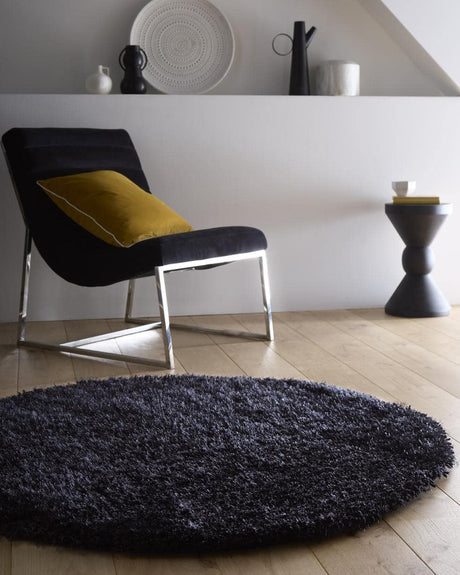 Round Shaggy Rug in dark colour, placed under a chair in a stylish living room setting