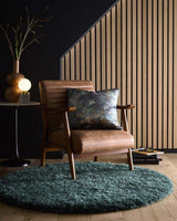 Modern round shaggy rug in teal colour placed under a stylish armchair and decorative objects