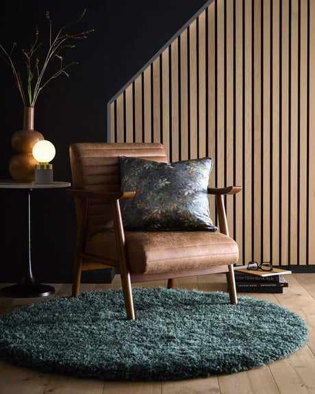 Modern round shaggy rug in teal colour placed under a stylish armchair and decorative objects