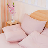 SHEET STORY Soft Pink Bedding Set with Decorative Cushions and Floral Accent on Bedside Table