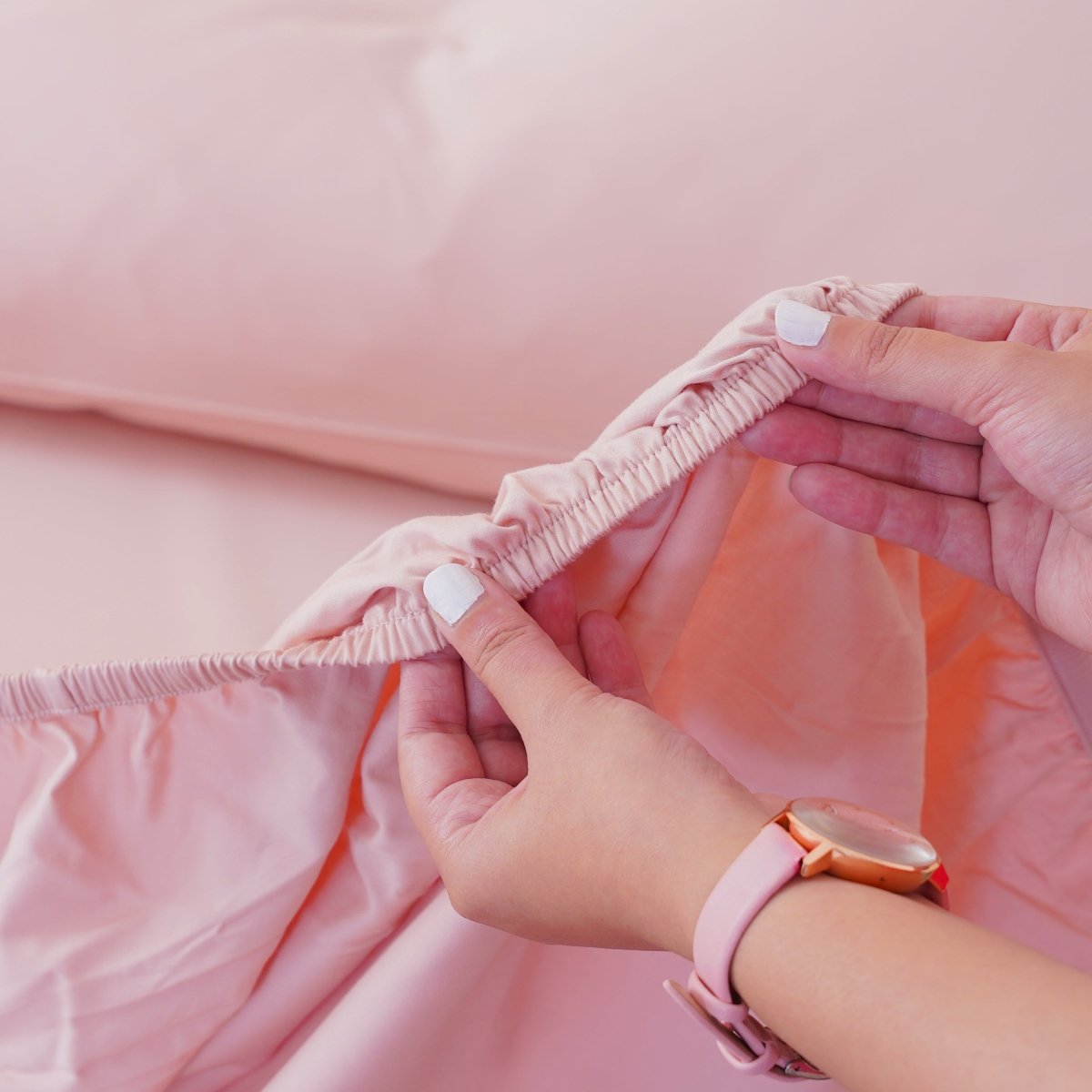 Smooth pink fitted sheet being adjusted, showcasing the perfect fit for a comfortable bed