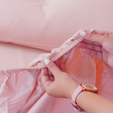 Smooth pink fitted sheet being adjusted, showcasing the perfect fit for a comfortable bed