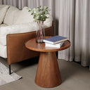 Wooden side table with a conical base, books and a vase on top, styled next to a sofa