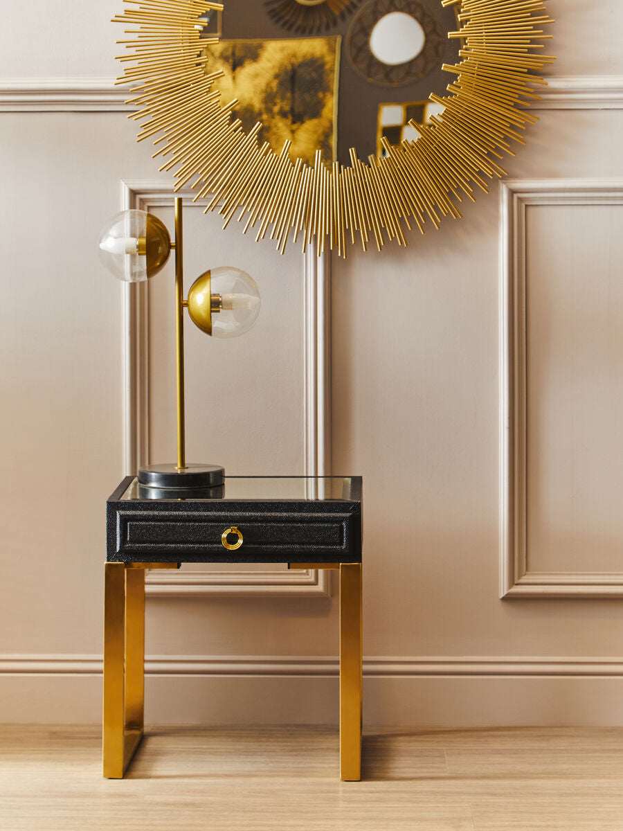 Orsina black side table with a single drawer and golden legs, styled with a decorative lamp and mirror