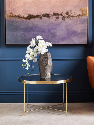Modern Orsina Side Table with a Gold Base and Glass Top, featuring a flower vase and wall art