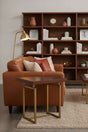 Orsina Side Table with a sleek wooden top and gold metal legs, placed beside a brown leather sofa