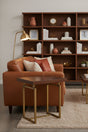 Orsina Side Table with a sleek wooden top and gold metal legs, placed beside a brown leather sofa