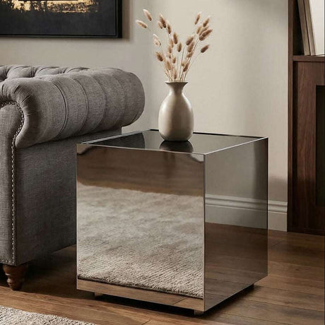 Orsina modern side table with a sleek mirrored finish beside a grey tufted sofa