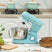 Wise Galleria Stand Mixer in teal with stainless steel bowl and whisk attachment on kitchen counter