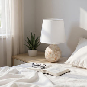 MSL Table Lamp with a textured base and a white shade placed on a bedside table with a plant and book
