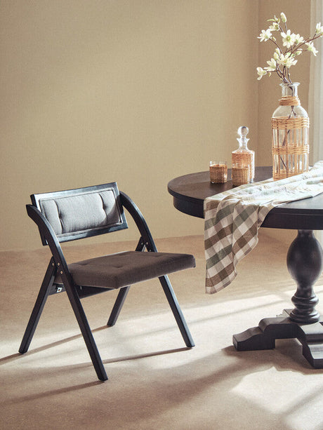 Orsina Tablecloth in a chic design draped over a round table with a black chair and decorative vase