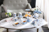 Elegant tea set with floral design on a marble table next to a cake stand displaying treats