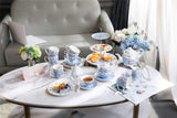 Elegant tea set with floral design on a marble table next to a cake stand displaying treats