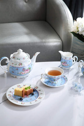 Elegant tea cups with a matching teapot and plate featuring cakes on a marble table