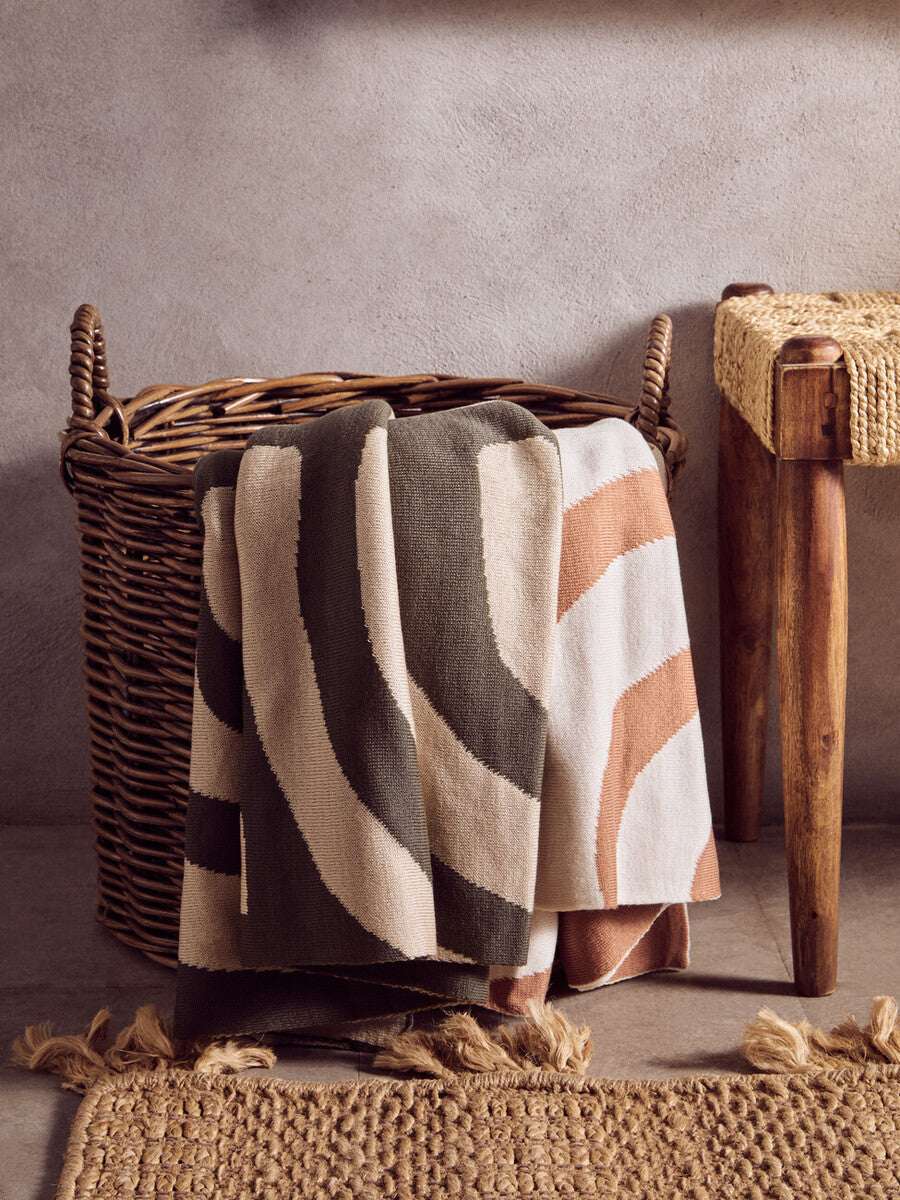 Orsina Terracotta Throw with a modern abstract pattern draped over a woven basket