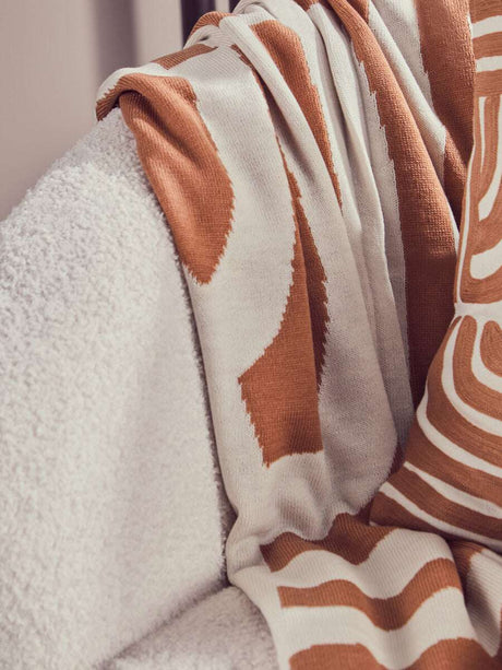 Orsina Terracotta Throw draped over a soft white armchair, featuring a stylish design