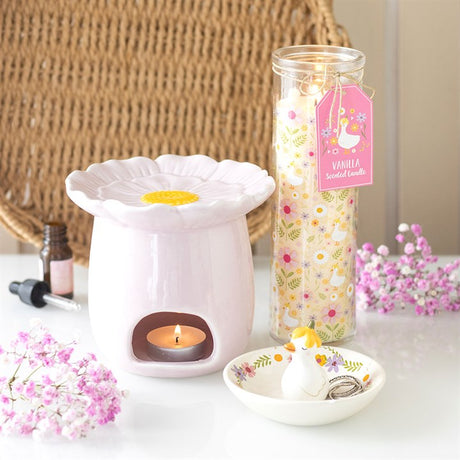 Pink ceramic oil burner with a flower design, surrounded by vanilla scented candle and decorative elements