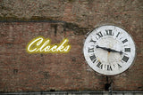 Widdop Wall Clock with Roman Numerals against a brick wall and neon Clocks sign
