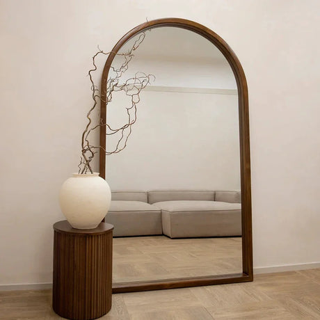 Elegant wall mirror with an arched design and a wooden frame, featuring a stylish vase and natural decor