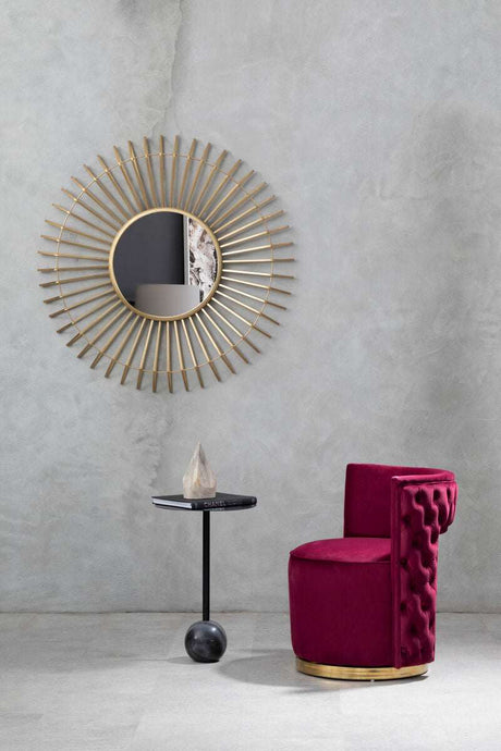 Orsina Wall Mirror with Radiant Gold Sunburst Design Above a Stylish Burgundy Chair and Black Side Table