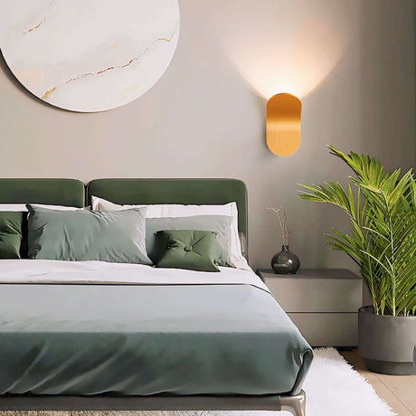 Nisu Home Wall Sconce in gold finish illuminating a stylish bedroom with a circular wall art