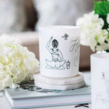 Avalon Home UK Wax Glass Candle featuring elegant artwork and surrounded by decorative flowers