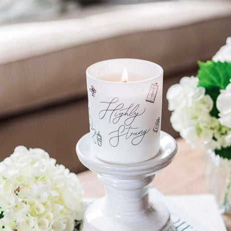 Avalon Home UK Wax Glass Candle in decorative holder with a warm flame and floral arrangement
