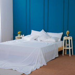 SHEET STORY Flat Sheet in crisp white draped over a bed with stylish pillows and a vibrant blue wall