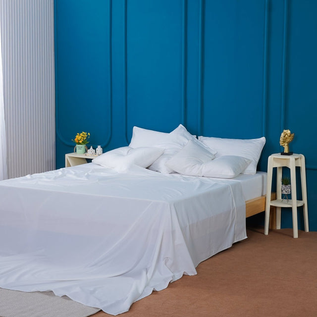SHEET STORY Flat Sheet in crisp white draped over a bed with stylish pillows and a vibrant blue wall
