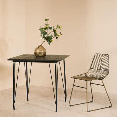 Orsina Wire Chair beside a minimalist black table with a vase of greenery