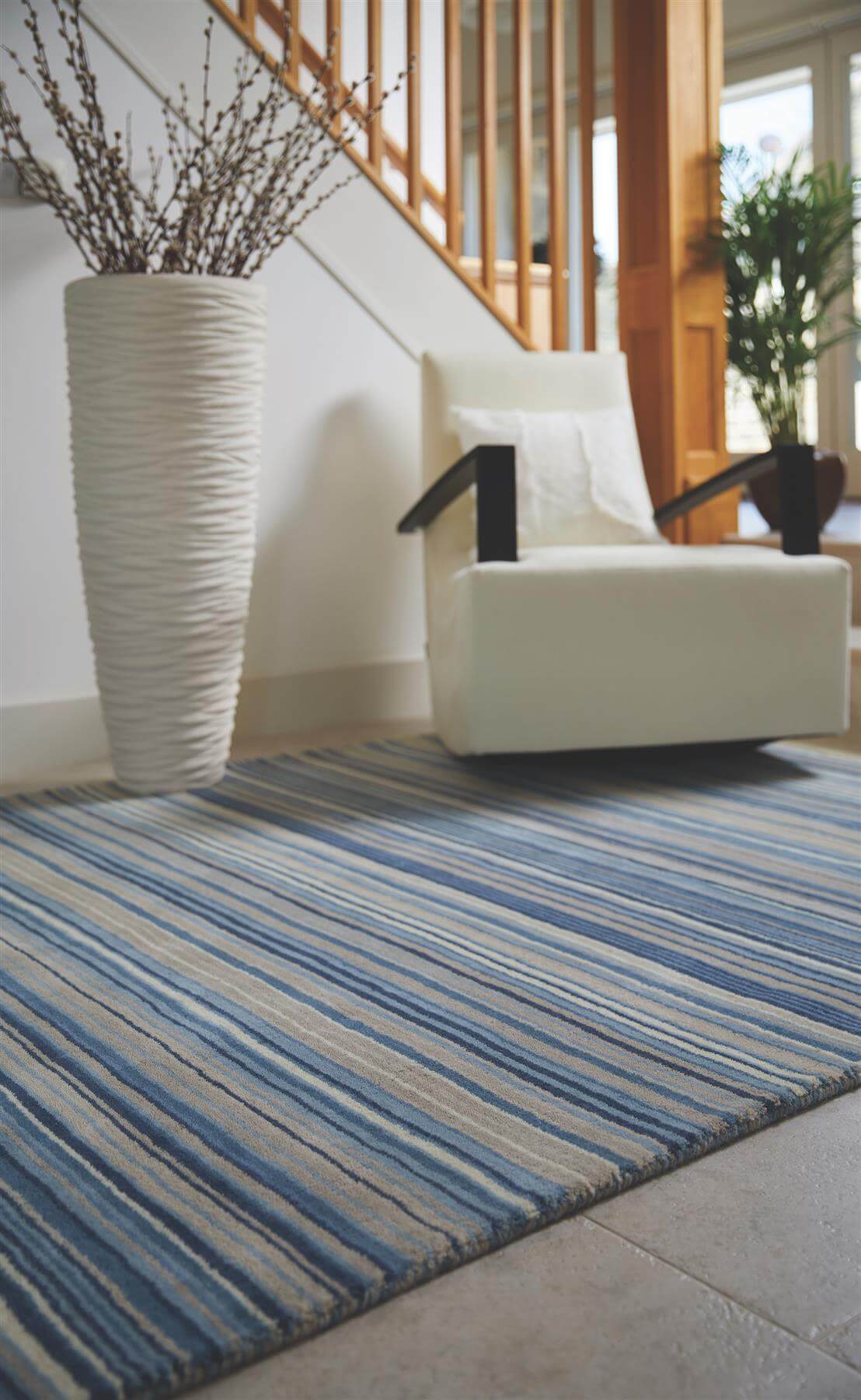 Striped blue and beige wool rug placed under a chair and vase for a stylish interior