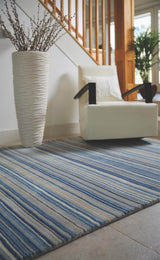 Striped blue and beige wool rug placed under a chair and vase for a stylish interior