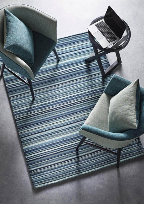 Blue and grey striped wool rug placed under modern chairs and a side table with a laptop