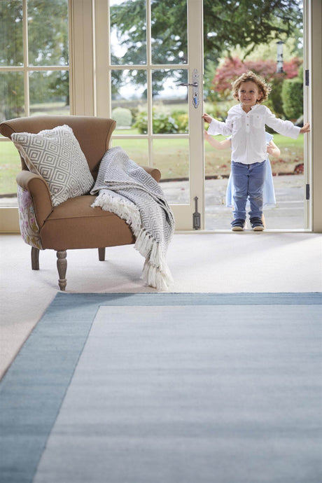 Light blue wool rug in a spacious living area with a child standing by the door