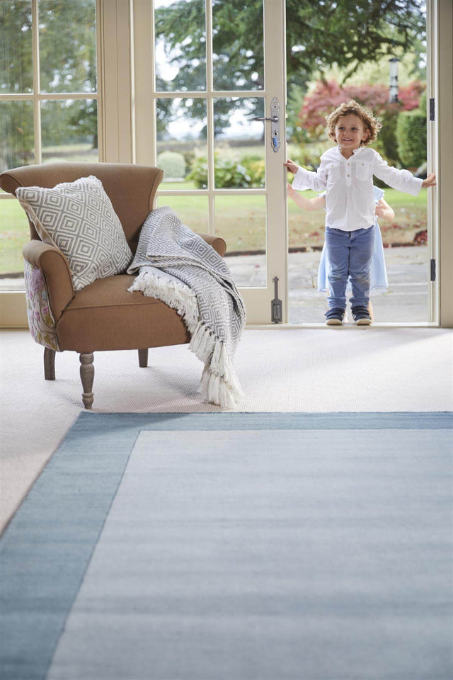 Light blue wool rug in a spacious living area with a child standing by the door