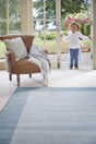 Light blue wool rug in a spacious living area with a child standing by the door