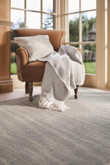 Elegant wool rug positioned on a wooden floor with a comfy chair and patterned throw blanket